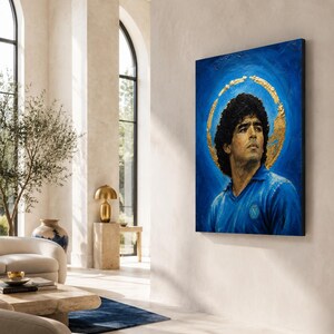 Puede incluir: Una pieza de arte mural rectangular que muestra el retrato de un hombre con cabello oscuro y rizado, vistiendo una camisa azul con cuello y un emblema circular. El fondo es azul intenso con un halo de pan de oro texturizado.