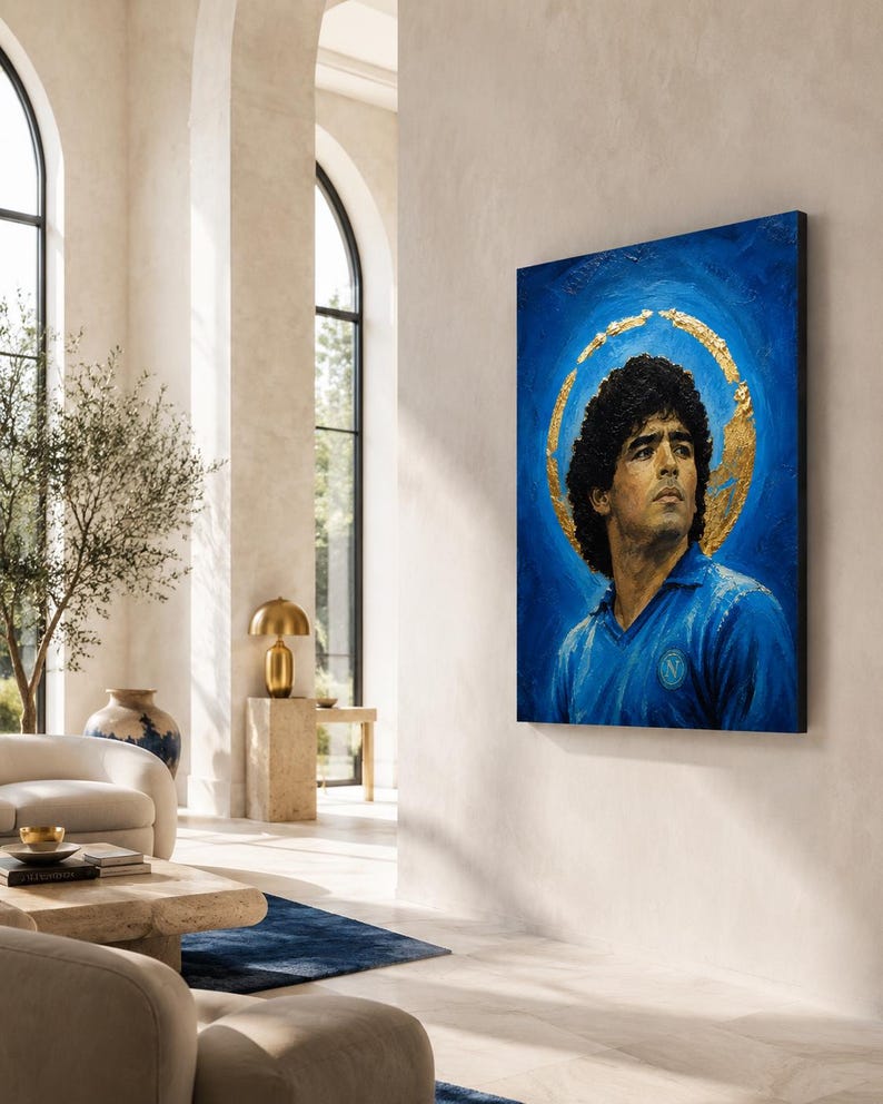 Puede incluir: Una pieza de arte mural rectangular que muestra el retrato de un hombre con cabello oscuro y rizado, vistiendo una camisa azul con cuello y un emblema circular. El fondo es azul intenso con un halo de pan de oro texturizado.