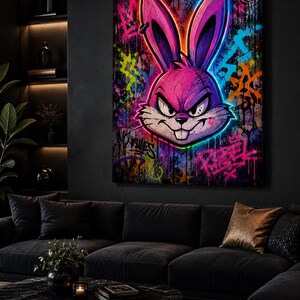 Peut inclure: Une &oelig;uvre d'art murale rectangulaire repr&eacute;sentant une t&ecirc;te de lapin violette stylis&eacute;e aux contours n&eacute;on avec une expression col&eacute;rique. Le fond est une surface sombre et textur&eacute;e couverte d'&eacute;claboussures de peinture graffiti et du mot Rebel en rose.