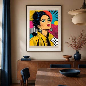 May include: A framed pop art print featuring a stylized illustration of a person with dark hair in an updo, wearing a yellow collared jacket and large circular earrings. The background incorporates vibrant geometric patterns, dots, and bold colors.