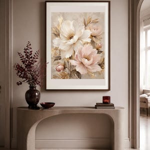 May include: A framed wall art print featuring a soft-toned floral painting of large white and pale pink peonies with golden accents. The artwork is displayed in a dark brown frame and hangs on a neutral-colored wall above a curved console table.