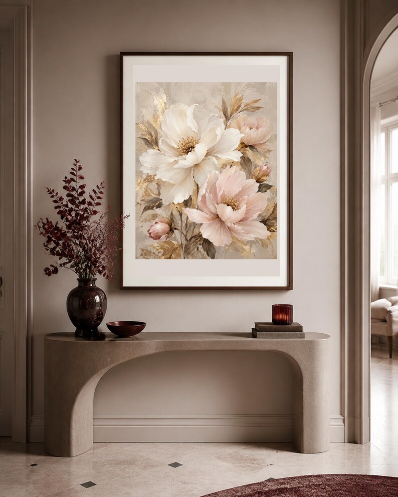 May include: A framed wall art print featuring a soft-toned floral painting of large white and pale pink peonies with golden accents. The artwork is displayed in a dark brown frame and hangs on a neutral-colored wall above a curved console table.