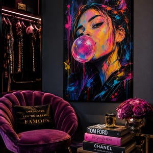 Puede incluir: Un lienzo vibrante que muestra a una persona soplando una burbuja de chicle rosa, con salpicaduras de pintura ne&oacute;n en azul, amarillo y rosa. La obra se exhibe en una habitaci&oacute;n con un sill&oacute;n de terciopelo morado y un coj&iacute;n negro con texto dorado.