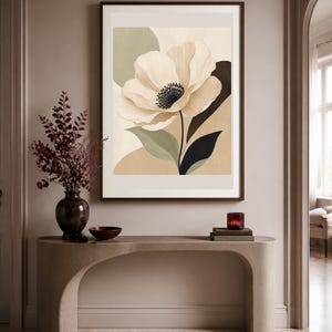 K&ouml;nnte beinhalten: Ein gerahmter Kunstdruck mit einer gro&szlig;en, stilisierten cremefarbenen Blume mit dunkler Mitte, vor abstrakten Formen in gedeckten Salbeigr&uuml;n-, Beige- und Dunkelbraunt&ouml;nen. Das Kunstwerk befindet sich in einem dunkelbraunen Rahmen an der Wand.