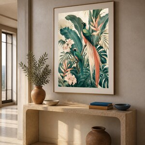 Puede incluir: Una impresi&oacute;n de arte mural vertical enmarcada que muestra dos aves quetzal posadas entre un exuberante follaje tropical, incluyendo grandes hojas de monstera verde oscuro, hojas de palma y flores de hibisco rosa p&aacute;lido sobre un fondo crema.