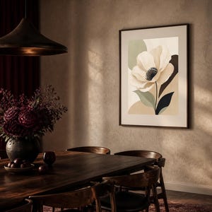 K&ouml;nnte beinhalten: Ein gerahmter Kunstdruck mit einer gro&szlig;en, stilisierten cremefarbenen Blume mit dunkler Mitte, vor abstrakten Formen in gedecktem Salbeigr&uuml;n, Beige und Anthrazit, pr&auml;sentiert in einem schmalen dunklen Rahmen an einer strukturierten Wand.