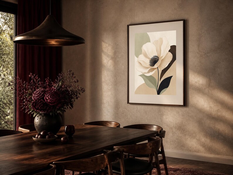 K&ouml;nnte beinhalten: Ein gerahmter Kunstdruck mit einer gro&szlig;en, stilisierten cremefarbenen Blume mit dunkler Mitte, vor abstrakten Formen in gedecktem Salbeigr&uuml;n, Beige und Anthrazit, pr&auml;sentiert in einem schmalen dunklen Rahmen an einer strukturierten Wand.