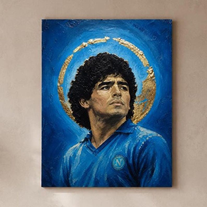 Puede incluir: Un cuadro rectangular sobre lienzo que muestra el retrato de un hombre de pelo oscuro y rizado con una camisa de cuello azul y un emblema circular en el pecho. Un halo dorado texturizado rodea la cabeza sobre un fondo azul intenso.