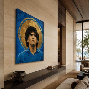 Puede incluir: Un cuadro rectangular sobre lienzo que muestra el retrato de un hombre de pelo rizado oscuro con una camisa azul de cuello. La figura se sit&uacute;a sobre un fondo azul vibrante con un gran halo circular dorado y texturizado alrededor de la cabeza.