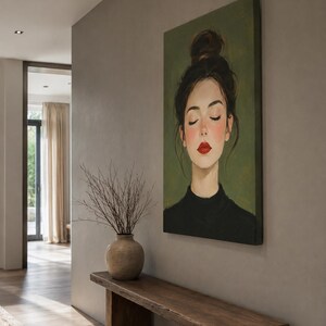 Puede incluir: Un cuadro rectangular sobre lienzo que muestra el retrato de una persona con los ojos cerrados, el cabello oscuro recogido en un mo&ntilde;o alto y labios pintados de rojo intenso. Viste una prenda negra sobre un fondo verde oliva apagado.