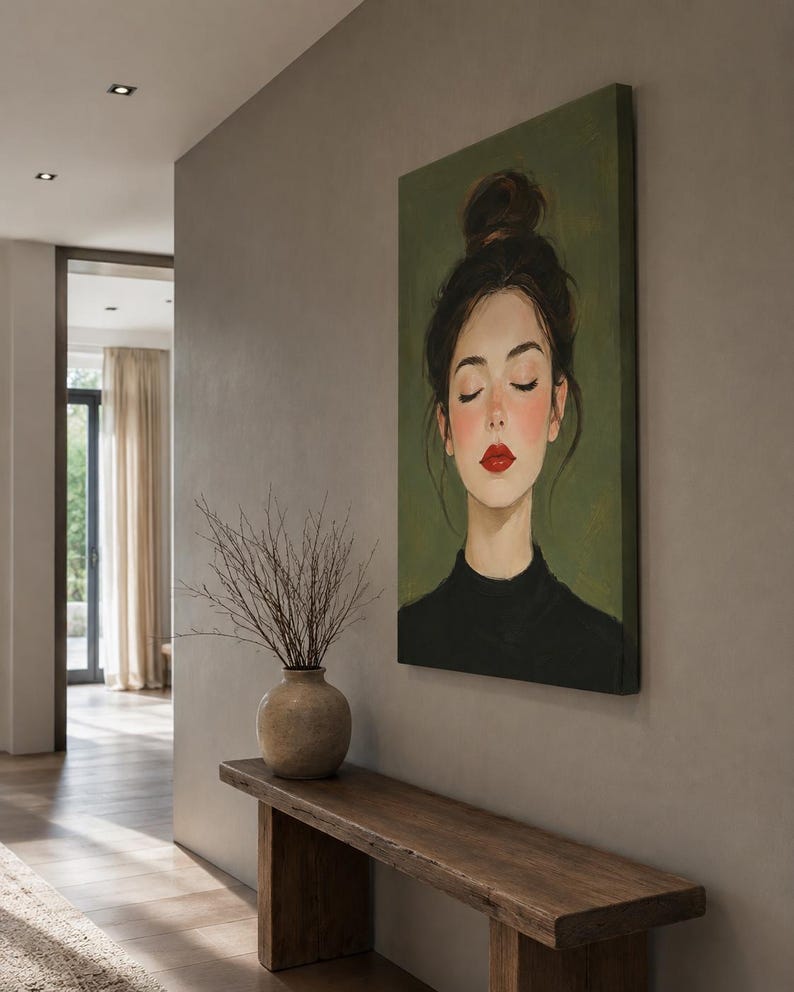 Puede incluir: Un cuadro rectangular sobre lienzo que muestra el retrato de una persona con los ojos cerrados, el cabello oscuro recogido en un mo&ntilde;o alto y labios pintados de rojo intenso. Viste una prenda negra sobre un fondo verde oliva apagado.