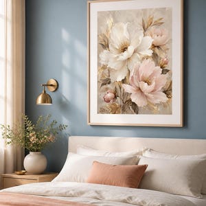 May include: A framed wall art print featuring a bouquet of large white and soft pink peony flowers with golden accents, displayed in a light wood frame. The artwork is hung on a blue wall above a bed with white bedding and a peach-colored throw.