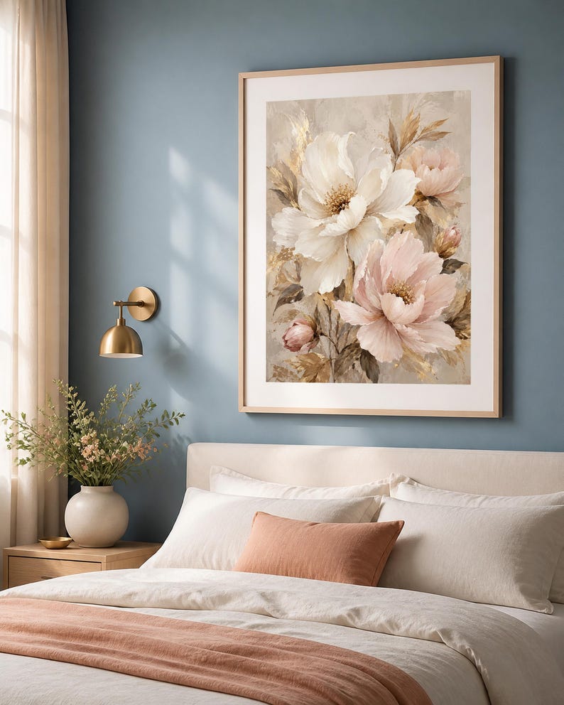 May include: A framed wall art print featuring a bouquet of large white and soft pink peony flowers with golden accents, displayed in a light wood frame. The artwork is hung on a blue wall above a bed with white bedding and a peach-colored throw.