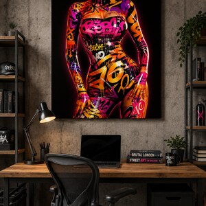 Puede incluir: Una impresi&oacute;n de arte mural cuadrada que muestra un torso con un body ajustado y brillante cubierto de arte callejero estilo grafiti. El dise&ntilde;o incluye salpicaduras de pintura rosa, naranja y amarilla, etiquetas y letras abstractas sobre un fondo negro.