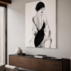 May include: A large rectangular wall art print featuring a black and white illustration of a person seen from the back. The figure wears a black slip dress with thin straps and a draped white garment over the shoulders, with dark hair in a bun.