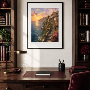 Peut inclure: Une impression d'art mural verticale encadr&eacute;e repr&eacute;sentant un village c&ocirc;tier &agrave; flanc de falaise au coucher du soleil. La sc&egrave;ne montre des escaliers en pierre, des fleurs roses et des b&acirc;timents surplombant une mer bleue sous un ciel dor&eacute;, dans un cadre noir.