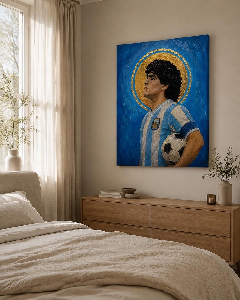May include: A rectangular canvas painting depicting a man with dark curly hair wearing a light blue and white striped soccer jersey, holding a black and white soccer ball, set against a vibrant blue background with a circular gold halo.
