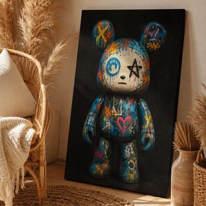 Op de afbeelding: Een rechthoekige canvasprint met een gestileerde berenfiguur tegen een effen zwarte achtergrond. De beer is versierd met levendige graffiti-achtige verfspatten, een roze hart, een zwarte ster en blauwe cirkelvormige markeringen.