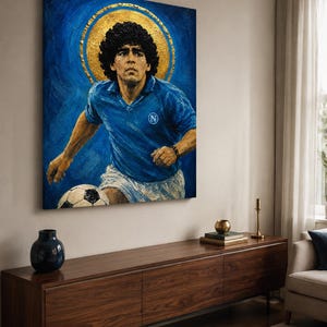 May include: A rectangular canvas painting depicting a soccer player with curly dark hair wearing a blue jersey with a white N logo and white shorts. The player is positioned in front of a large gold circular halo against a textured blue background.