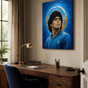 Puede incluir: Un cuadro rectangular sobre lienzo que muestra el retrato de un hombre de cabello oscuro y rizado con una camiseta azul de cuello. La figura se sit&uacute;a sobre un fondo azul intenso con un efecto de halo circular dorado y texturizado.