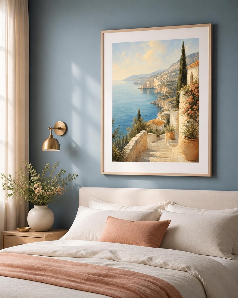 Puede incluir: Una impresi&oacute;n de arte mural vertical enmarcada que representa un paisaje costero mediterr&aacute;neo con escaleras de piedra, macetas de terracota y cipreses con vistas a un mar azul bajo un cielo suave, en un marco de madera clara con paspart&uacute;.