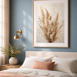 Pu&ograve; includere: Una grande stampa da parete rettangolare che raffigura una composizione di erba della pampa, cardi e fiori di campo essiccati nei toni del beige e del crema. L'opera &egrave; racchiusa in una cornice di legno chiaro su una parete blu tenue.