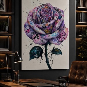 Puede incluir: Un lienzo rectangular para pared que presenta una gran rosa morada central cubierta con etiquetas, s&iacute;mbolos y texto coloridos al estilo grafiti. La obra incluye salpicaduras de pintura negra sobre un fondo blanco, con un tallo y hojas de color verde oscuro.