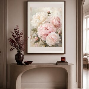Puede incluir: Una l&aacute;mina de arte enmarcada que muestra un ramo de peon&iacute;as de color rosa suave y crema con hojas verdes. La obra est&aacute; expuesta en un marco marr&oacute;n oscuro colgado en una pared de tonos neutros sobre una mesa consola curva y clara.