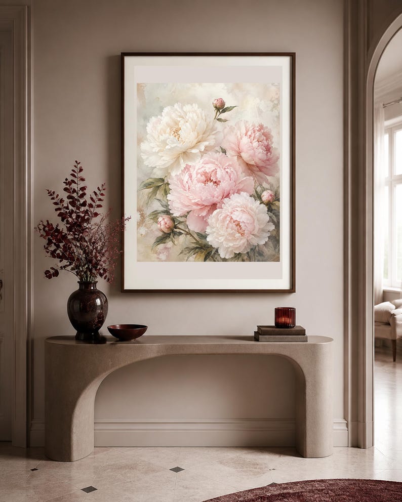 Puede incluir: Una l&aacute;mina de arte enmarcada que muestra un ramo de peon&iacute;as de color rosa suave y crema con hojas verdes. La obra est&aacute; expuesta en un marco marr&oacute;n oscuro colgado en una pared de tonos neutros sobre una mesa consola curva y clara.