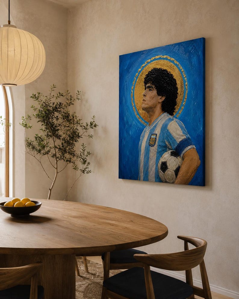 May include: A rectangular canvas painting featuring a portrait of a soccer player with dark curly hair, wearing a light blue and white striped jersey, holding a soccer ball, set against a vibrant blue background with a circular gold halo.