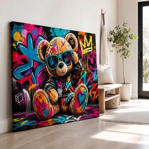 May include: A rectangular canvas print featuring a brown teddy bear wearing bright blue sunglasses and a dark jacket. The background is a vibrant graffiti-style mural with splashes of pink, blue, yellow, and black, including crown and heart motifs.