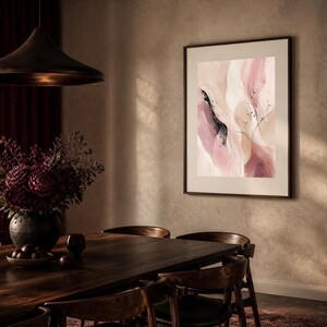 K&ouml;nnte beinhalten: Ein gerahmter abstrakter Wandkunstdruck mit flie&szlig;enden Formen in sanften Nuancen von Puderrosa, Creme und dunklem Mauve, akzentuiert durch feine, tintenartige schwarze Linien und kleine dunkle Sprenkel, pr&auml;sentiert in einem schmalen, dunklen Rahmen.