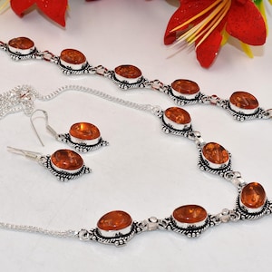 May include: A jewelry set consisting of a necklace, a bracelet, and a pair of earrings. Each piece features oval-shaped, translucent amber-colored stones set in silver-toned metal with intricate, textured detailing around the stone settings.