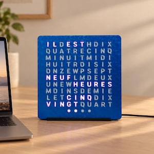 Op de afbeelding: Een vierkante blauwe woordklok met een raster van verlichte Franse letters die de tijd weergeven. De wijzerplaat bevat rijen letters waarbij specifieke woorden wit oplichten om de tijd aan te geven, met vier cirkelvormige stippen aan de onderkant.