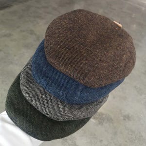 May include: Four different tweed flat caps stacked on top of each other. The top cap is brown, the next is blue, the next is gray, and the bottom cap is green.