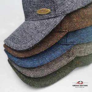 May include: A stack of five tweed caps in different colors, including gray, brown, blue, green, and black. The top cap has a small brass tag that reads "Grizzly Hatters Australia".