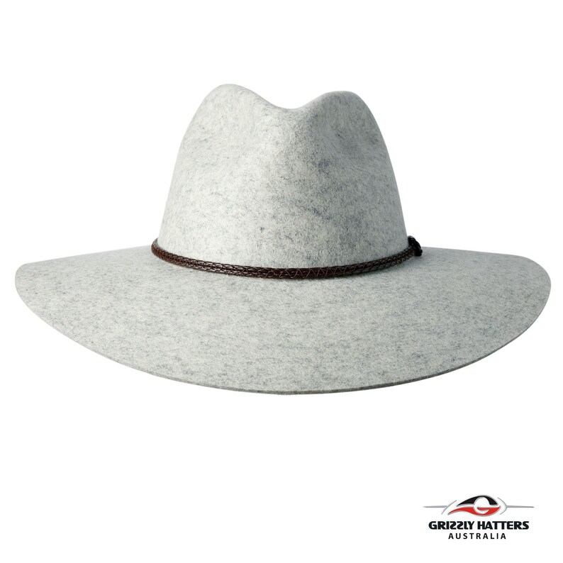 Op de afbeelding: Een lichtgrijze wollen fedora hoed met een bruin leren band. De hoed heeft een brede rand en een licht ingedeukte kroon.