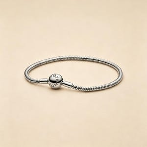 May include: A silver-toned snake chain bracelet featuring a spherical clasp. The round clasp is engraved with the text PANDORA in capital letters. The bracelet has a flexible, textured link design that forms a circular shape on a neutral background.