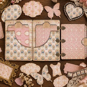 May include: A multi-page paper journal with a pink and blue patterned cover, featuring internal pockets and metal heart-shaped hinges. The set includes various die-cut paper shapes like butterflies, hearts, and labels, alongside a gold-toned frame.