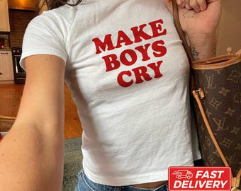 May include: A white short-sleeved t-shirt featuring the red text MAKE BOYS CRY printed on the front. The shirt is paired with a brown patterned tote bag. The text at the bottom indicates the model is wearing size XS and it is made with US cotton.