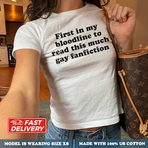 May include: A white short-sleeved t-shirt featuring black text printed on the chest that reads, First in my bloodline to read this much gay fanfiction. The shirt is made of 100% US cotton and is shown in a size XS fit with a crew neckline.