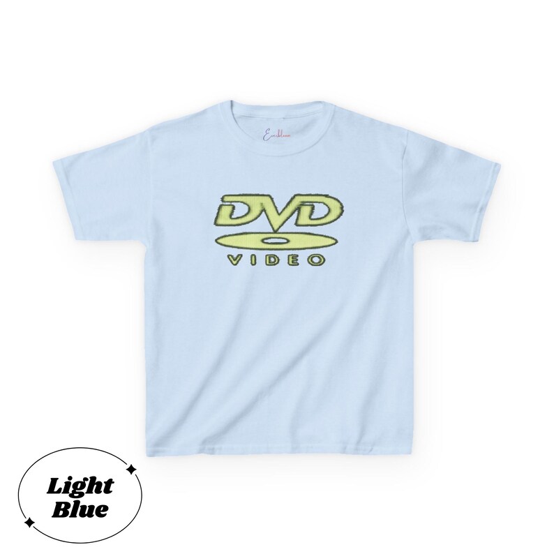 May include: A light blue short-sleeve t-shirt featuring a graphic on the chest. The graphic displays the text DVD in a stylized yellow font above a yellow disc icon and the word VIDEO in a smaller yellow font. The shirt has a crew neckline.