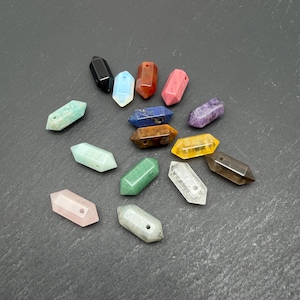 May include: A collection of fifteen double-terminated gemstone beads in various colors including black, white, red, pink, blue, purple, yellow, green, and clear. Each bead features a faceted hexagonal shape with a small hole drilled through the center.