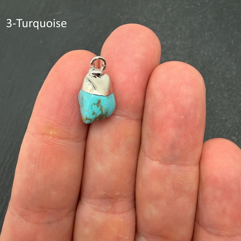 Pu&ograve; includere: Un piccolo ciondolo in pietra turchese irregolare con un cappuccio in metallo color argento e un occhiello circolare sulla parte superiore. La pietra presenta un colore blu brillante con venature marroni. Il testo 3-Turquoise &egrave; visibile in alto a sinistra.