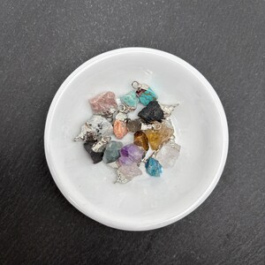 Pu&ograve; includere: Una collezione di piccoli ciondoli in pietre preziose grezze di vari colori, tra cui turchese, ametista, quarzo rosa e quarzo trasparente. Ogni pietra grezza &egrave; dotata di un gancio in metallo argentato sulla parte superiore come ciondolo.