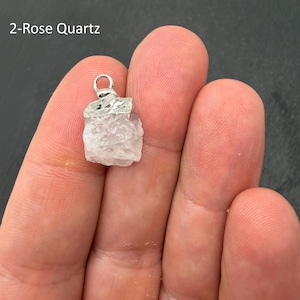 Pu&ograve; includere: Un ciondolo in quarzo rosa grezzo di colore rosa pallido con un cappuccio in metallo argentato testurizzato e un piccolo anello circolare. La pietra ha una forma cristallina irregolare ed &egrave; etichettata con il testo 2-Rose Quartz in alto a sinistra.