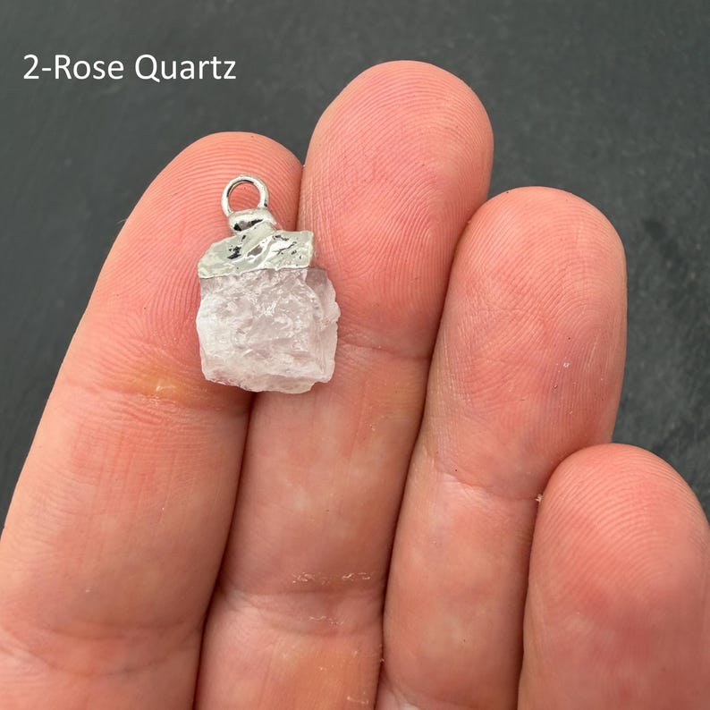 Pu&ograve; includere: Un ciondolo in quarzo rosa grezzo di colore rosa pallido con un cappuccio in metallo argentato testurizzato e un piccolo anello circolare. La pietra ha una forma cristallina irregolare ed &egrave; etichettata con il testo 2-Rose Quartz in alto a sinistra.