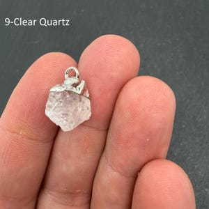 Pu&ograve; includere: Un ciondolo in quarzo chiaro grezzo, traslucido, con una forma irregolare e frastagliata, dotato di un gancio in metallo color argento sulla parte superiore. Il testo 9-Clear Quartz &egrave; visibile nell'angolo in alto a sinistra dell'immagine.