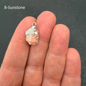 Pu&ograve; includere: Un ciondolo in pietra del sole grezza color pesca con una consistenza cristallina ruvida. La pietra &egrave; fissata da un cappuccio in metallo color argento con un piccolo anello circolare sulla parte superiore. Il testo 8-Sunstone &egrave; visibile.