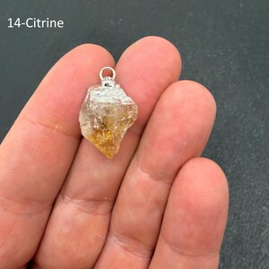 Pu&ograve; includere: Un ciondolo in cristallo di citrino grezzo caratterizzato da una pietra irregolare giallo-arancio traslucida con un cappuccio in metallo argentato e un piccolo anello circolare sulla parte superiore. Il testo 14-Citrine &egrave; visibile in alto a sinistra.